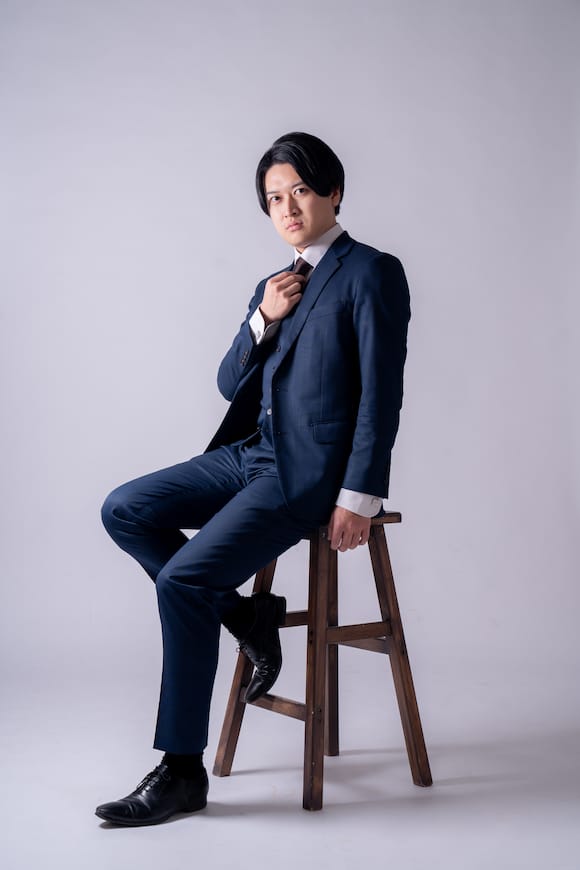 白背景でジャケット×白Tの着座ポートレート、親しみやすいSNSプロフィール写真