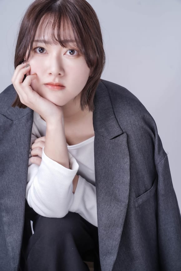 グレー背景でグレージャケット×白トップの着座ポートレート、落ち着いた印象のプロフィール写真