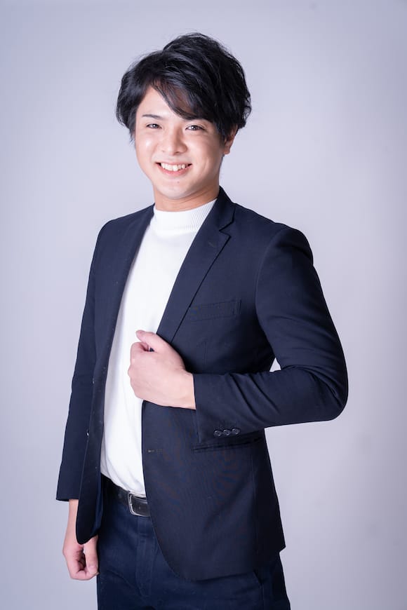 グレー背景でジャケット×白ニットの上半身ポートレート、企業サイト向けのプロフィール写真