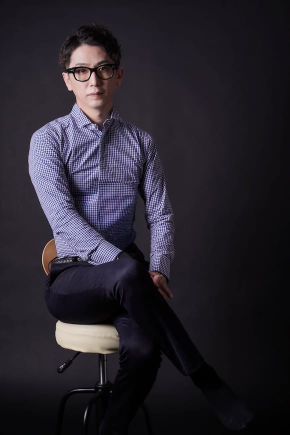 暗めの背景で椅子に座る全身ポートレート、クリエイター向けのプロフィール写真