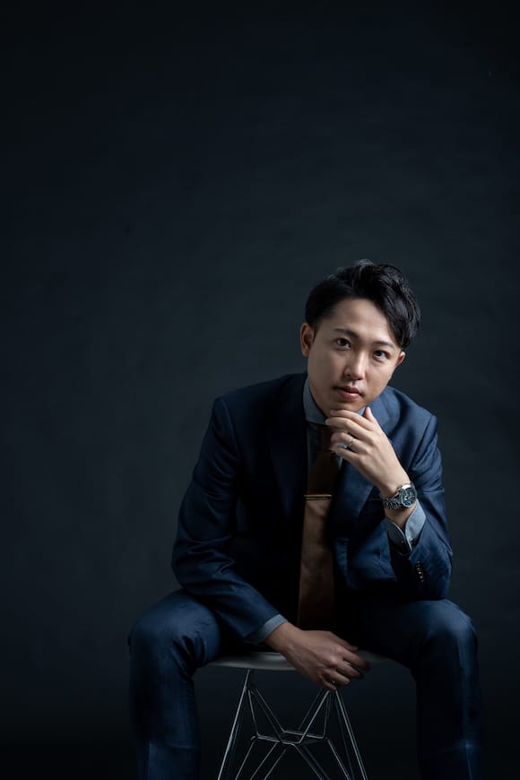 ダーク背景で前傾の着座ポートレート、広告用ビジュアル向けのシネマティック表現